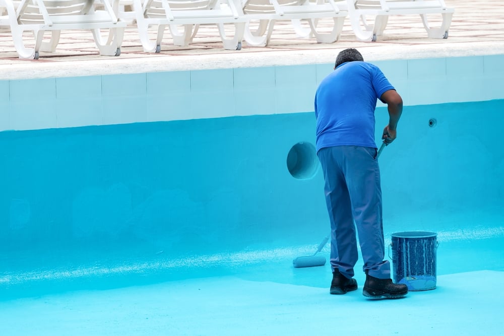 Unrecognizable,Worker,Repainting,Swimming,Pool,In,Blue,Colour.,Reconstruction,Process Maintenance worker in blue clothes paints the inside of a bright blue pool with a roller and nearby paint bucket.