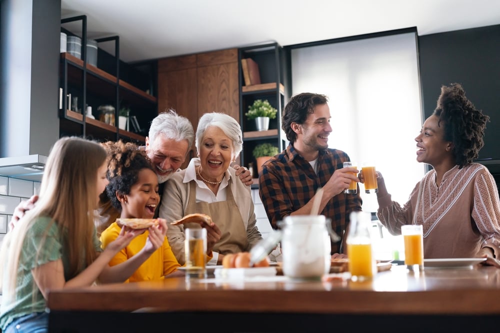 Happy,Multiethnic,Multigeneration,Family,With,Husband,,Wife,,Children,,Grandfather,And Multigenerational family toasting with orange juice around a kitchen table