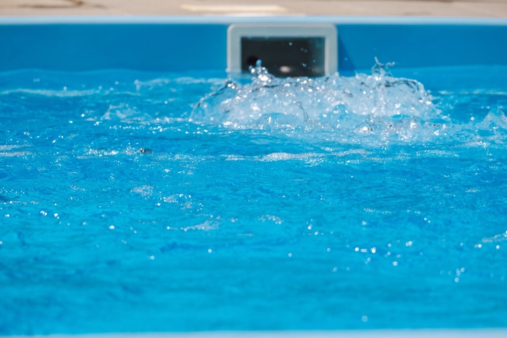 Clear,Blue,Water,Splashes,Near,A,Pool,Jet,,Indicating,Active Blue swimming pool with a return jet bubbling water near the far wall.